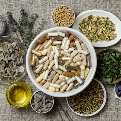 A table showing various dietary supplements surrounded by natural ingredients like herbs, nuts, oils, and fruits.