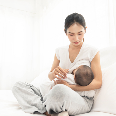 A young woman is sitting on a comfortable bed holding a baby to her breast