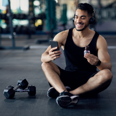 A man is sitting down, recovering from a workout at the gym, and is surrounded by workout equipment.