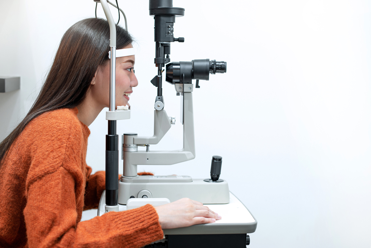 A young woman is sitting with her face in a slit lamp machine used to examine eyes.